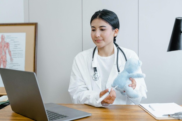 A female doctor giving an online consultation while demonstrating a health check on a stuffed toy, symbolizing care and wellness preparation for winter.